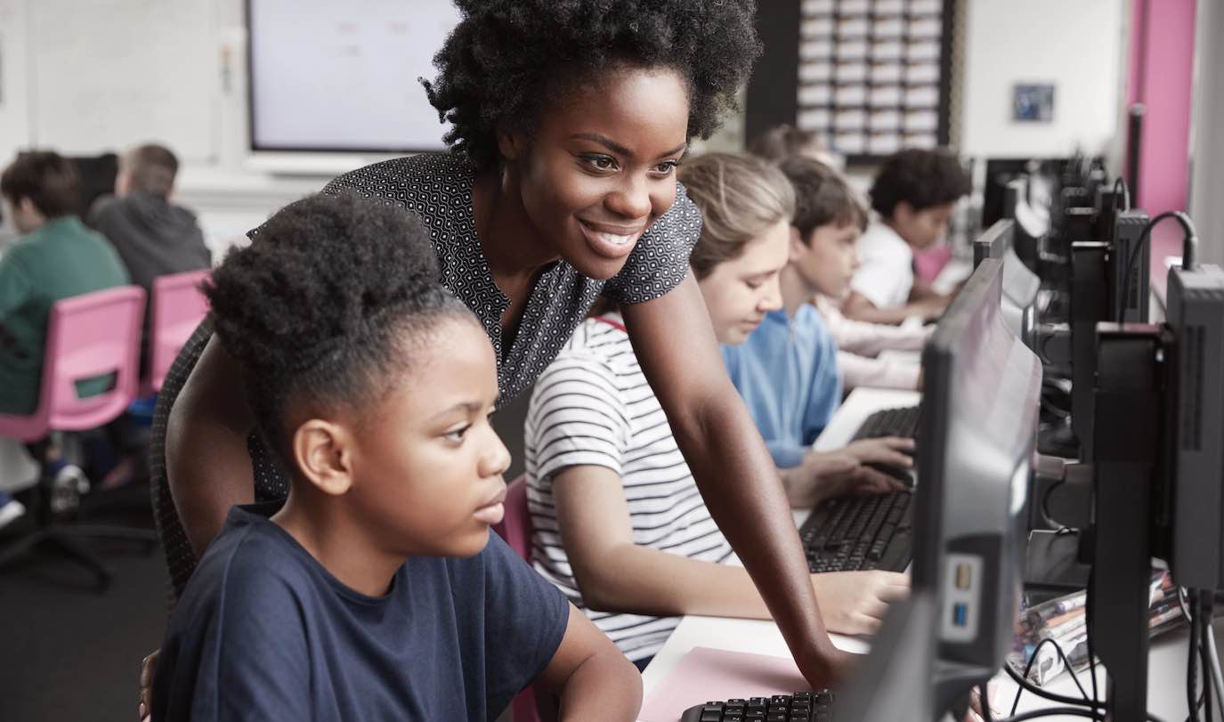 teacher helping students on computers in class
